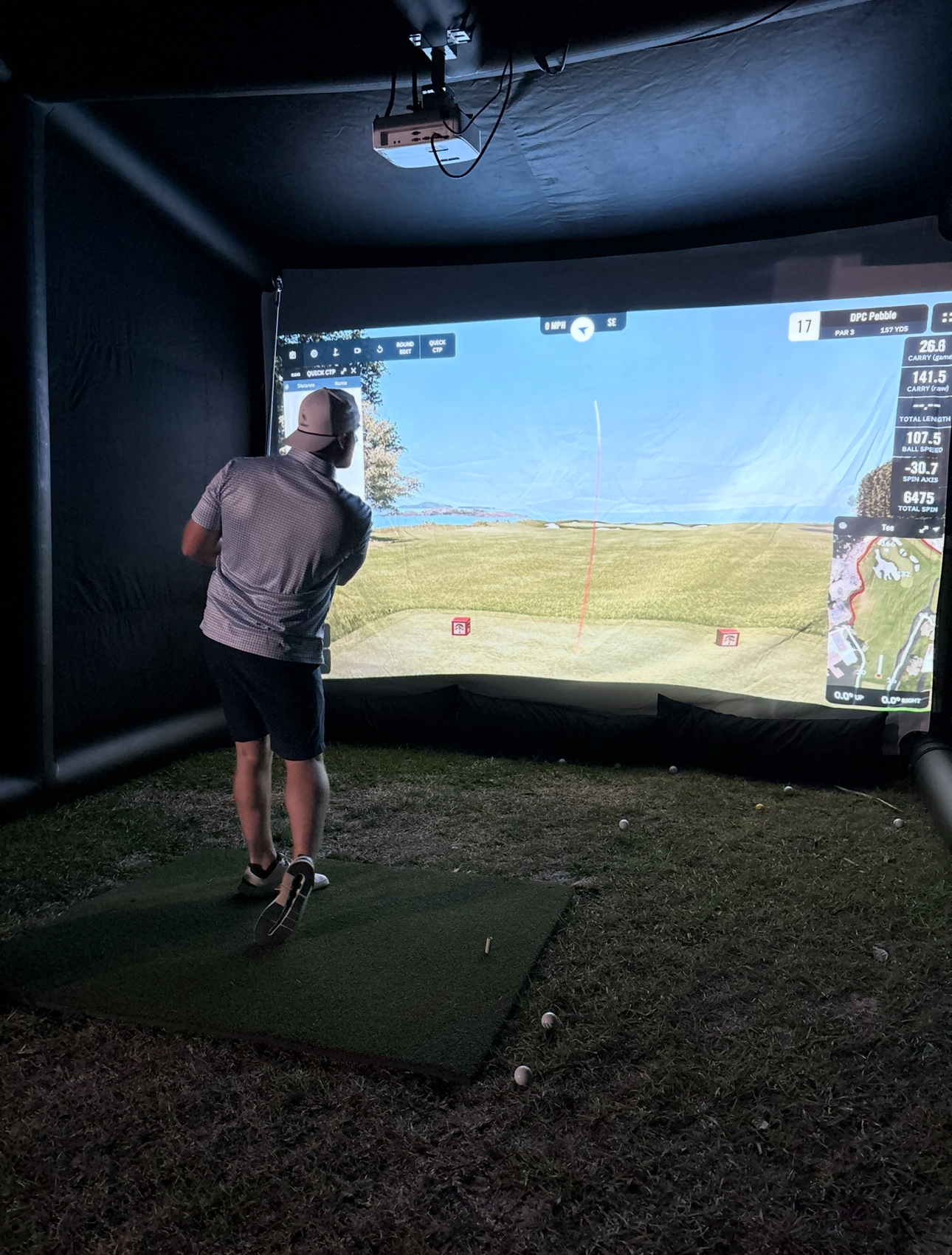 Player taking a swing inside an outdoor PopGolf simulator on the 17th at Pebble Beach