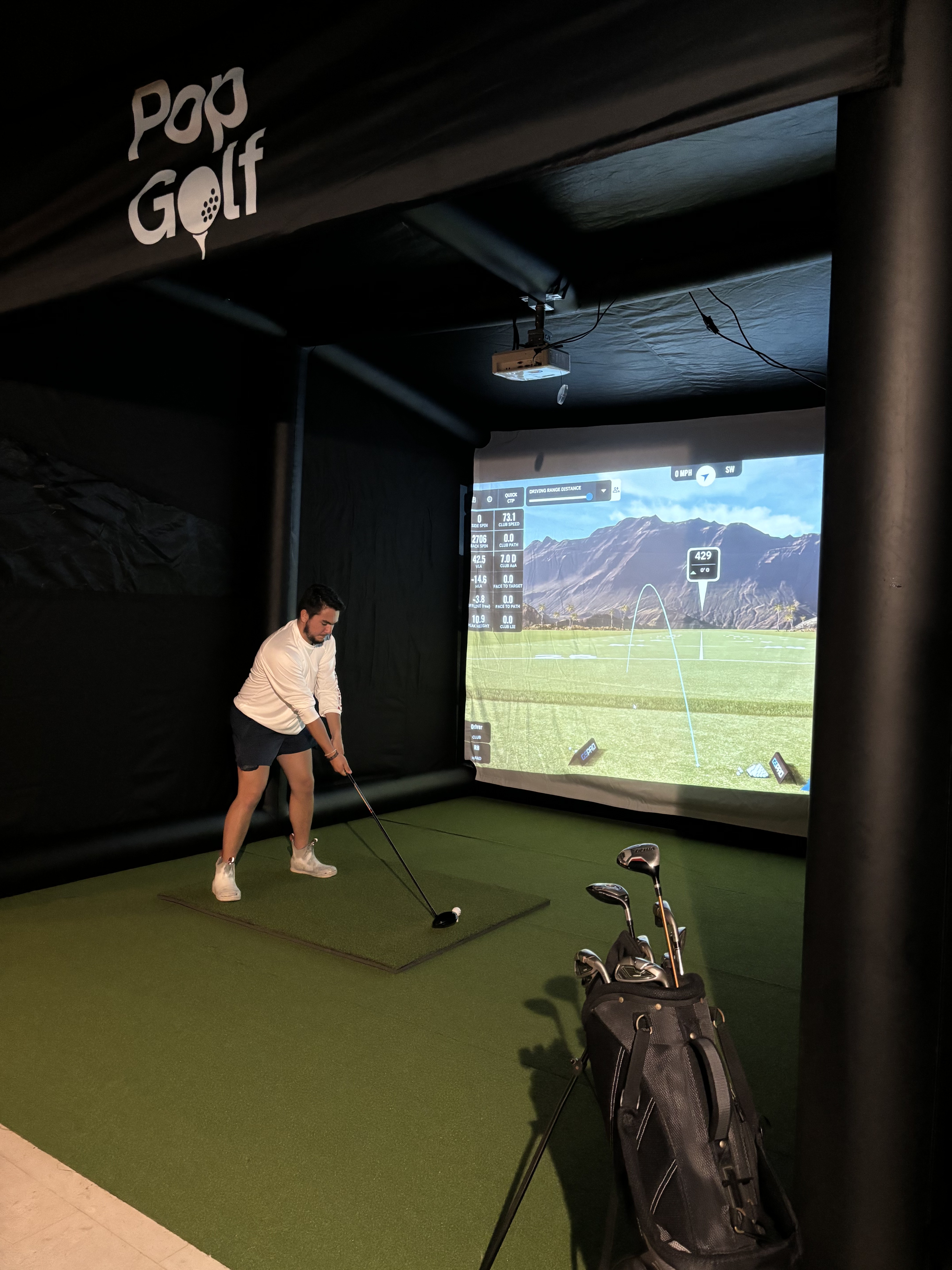 Guest taking a focused swing inside the PopGolf simulator at an indoor evening event