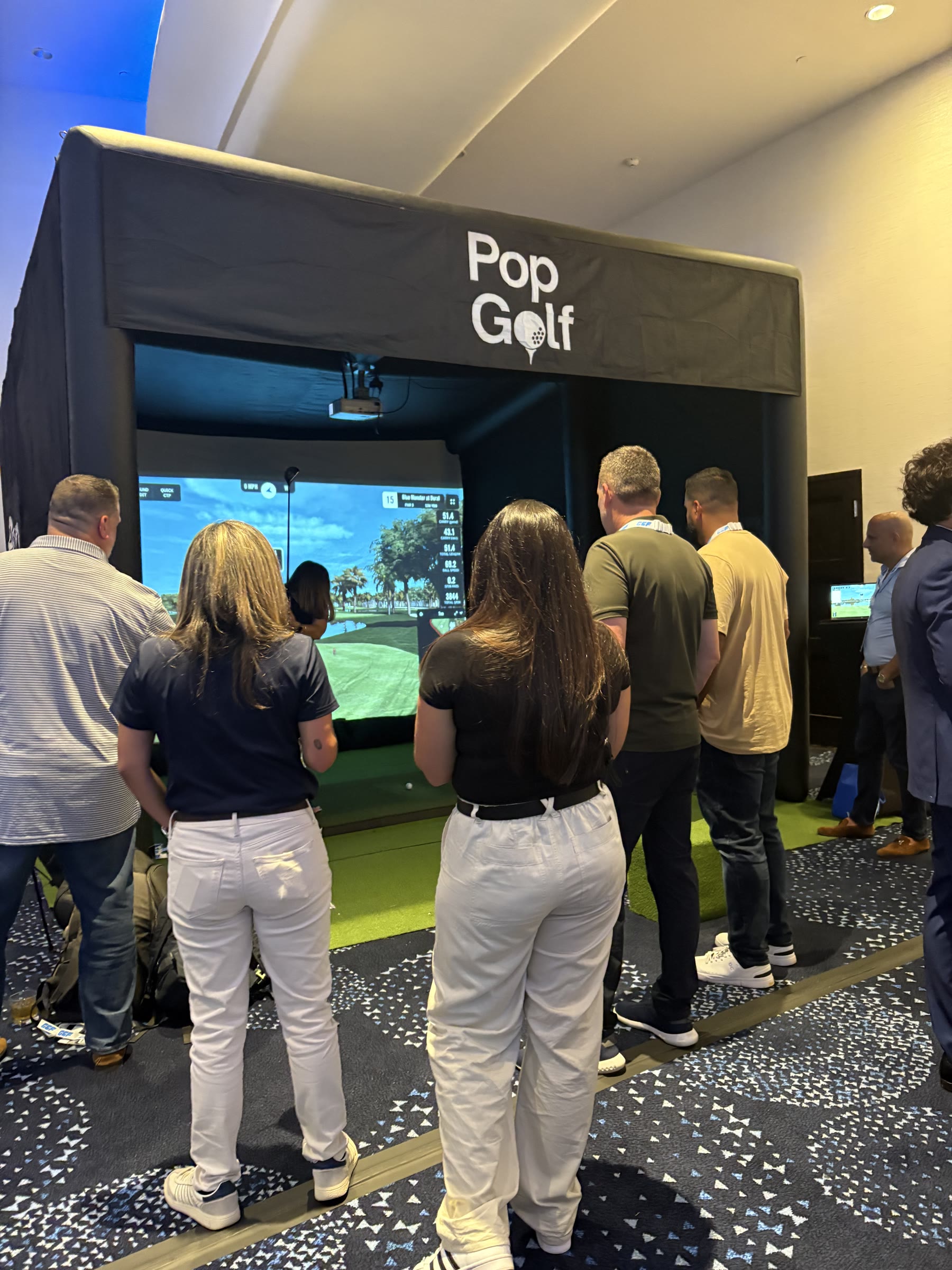 Attendees gathered in front of the PopGolf simulator during a conference