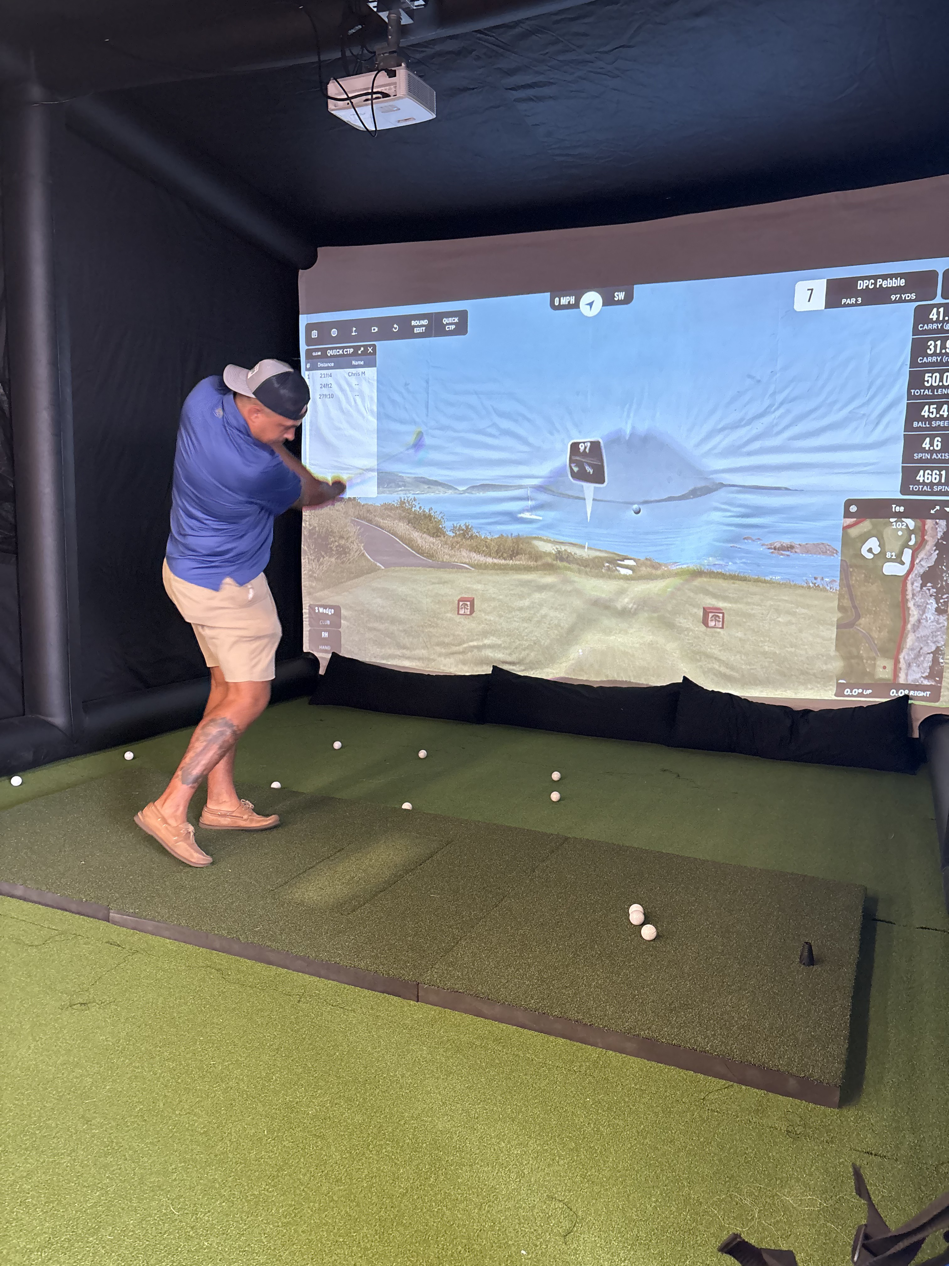 Guest mid-swing inside a PopGolf simulator playing Pebble Beach
