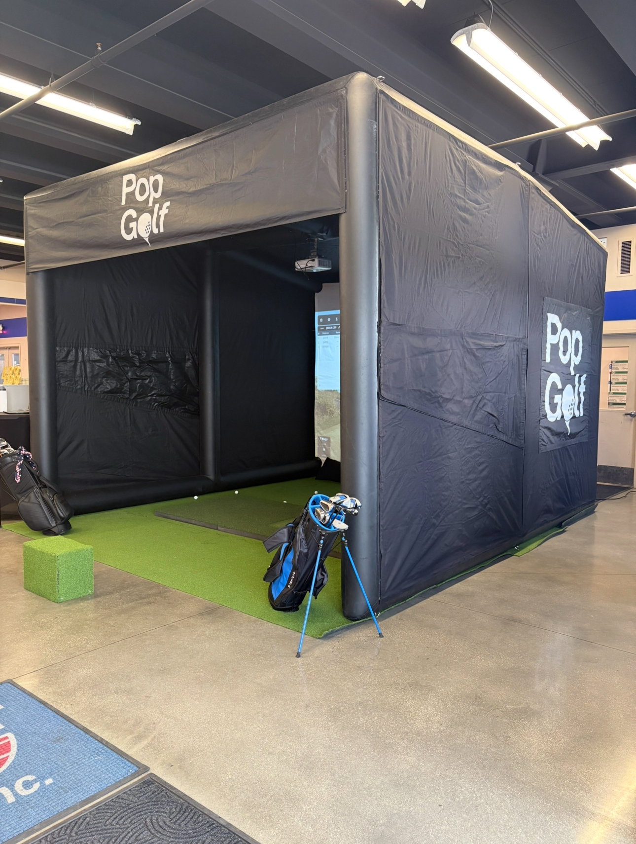 Turnkey PopGolf simulator installed inside an indoor venue with tee, mat, and clubs staged